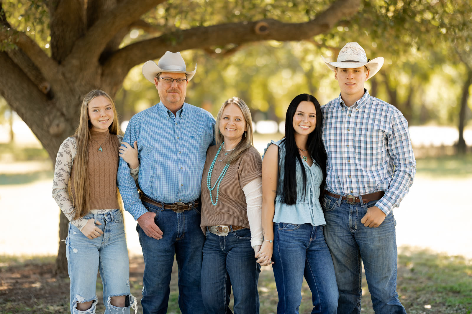 The Goodin family standing together under a big oak tree, in jeans and western shirts